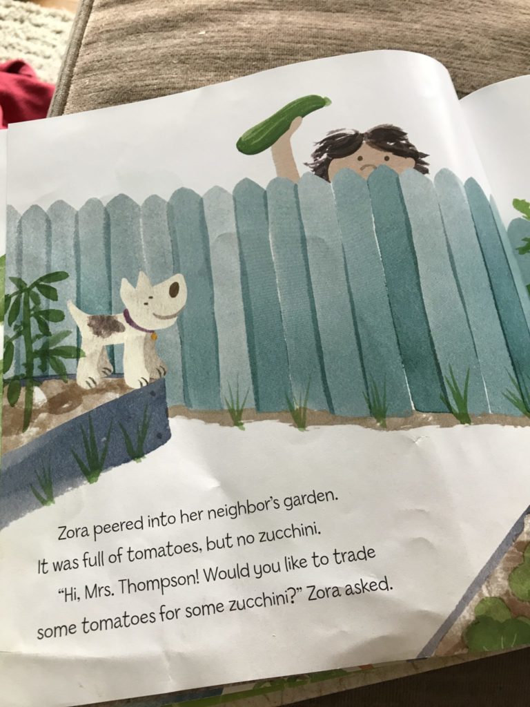 A book page featuring a girl behind a fence, holding a zucchini up over the fence.
