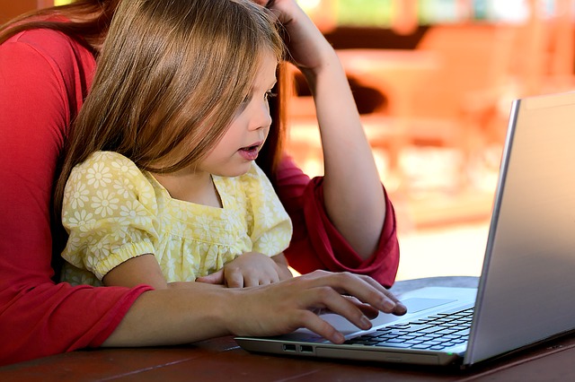 An image of a girl sitting on her mother's lap looking at a laptop screen