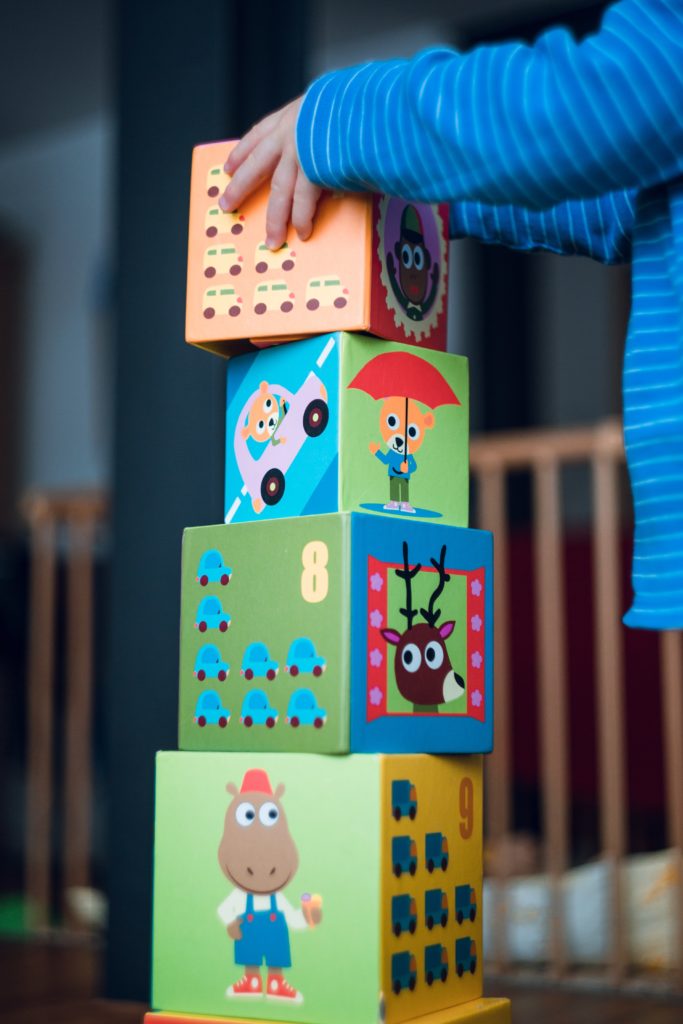 An image of a colorful block tower. A white child's hands are placing the last block on top.  The child's body and face are not visible.
