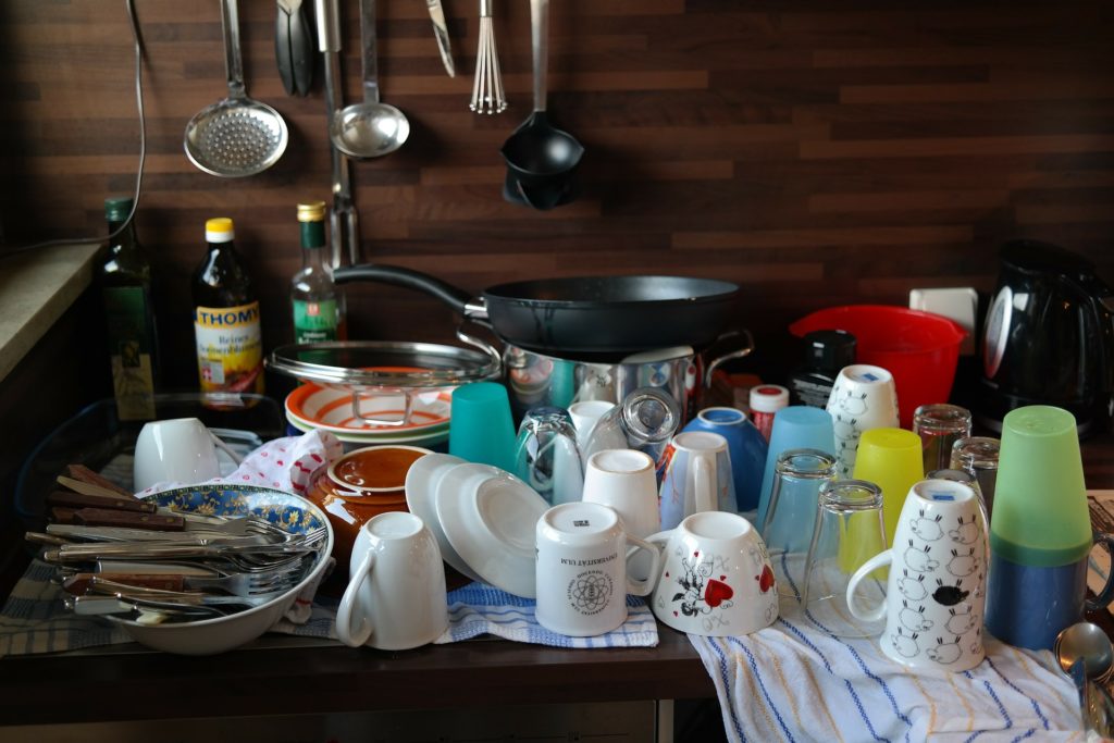 An image of a countertop covered in dishes, silverware, and cooking utensils.