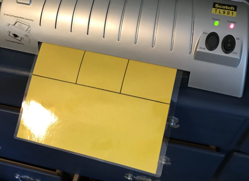 A photo of a Scotch brand laminator with a yellow visual schedule coming out of the laminator.