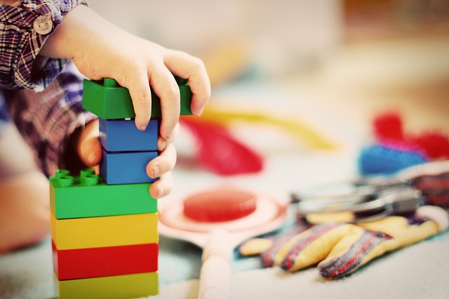 A photo of a child's hands. The hands are putting a lego type block on top of a tower.