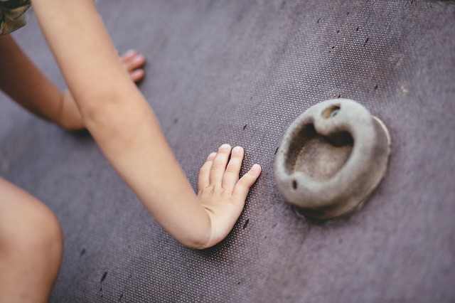 A child's hands and knee are visible on a climbing wall, along with a handhold.