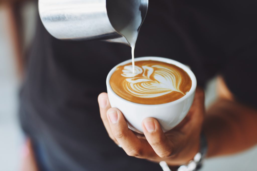 An image of milk being poured into a latte in a decorative floral pattern