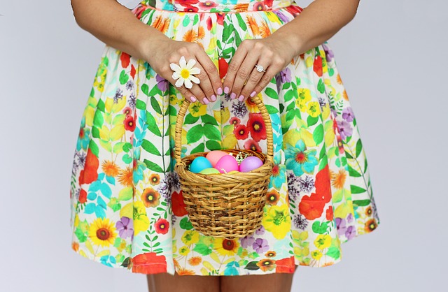 A person in a flowered dress holds an Easter basket with brightly colored eggs. 