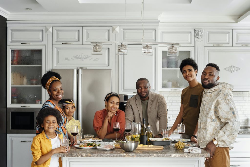 A Black family stands around an island with a large spread of food. 